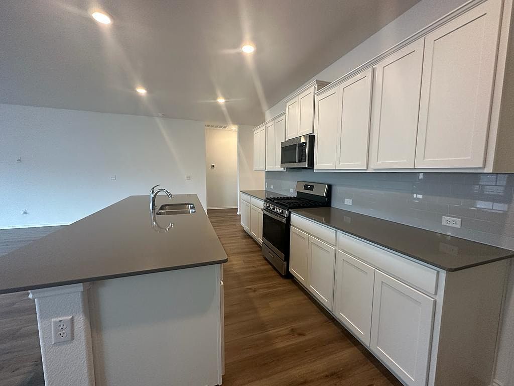 160 River Rise Road Kyle, TX 78640 - Photo 28 of 35 Kitchen featuring a large central island with an undermount sink, a stainless steel gas range, and a built-in microwave