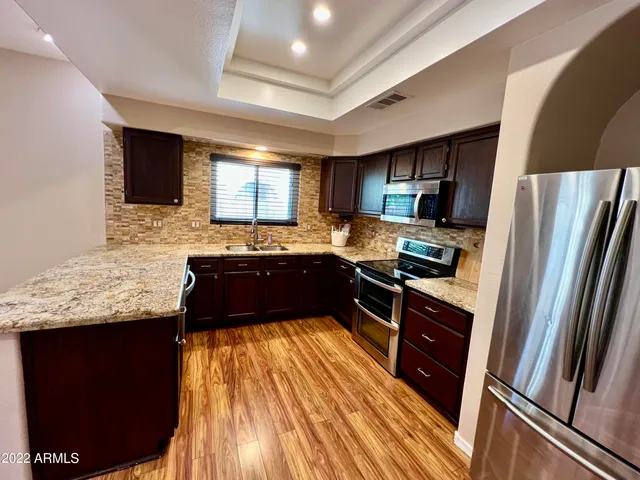 a kitchen with granite countertop stainless steel appliances a sink stove refrigerator and cabinets
