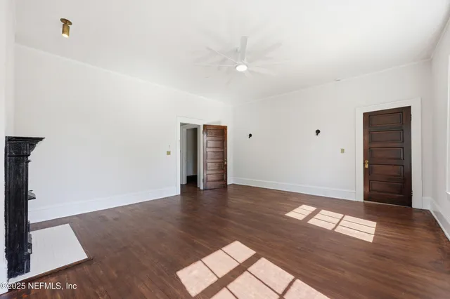 a view of an empty room with wooden floor and a ceiling fan