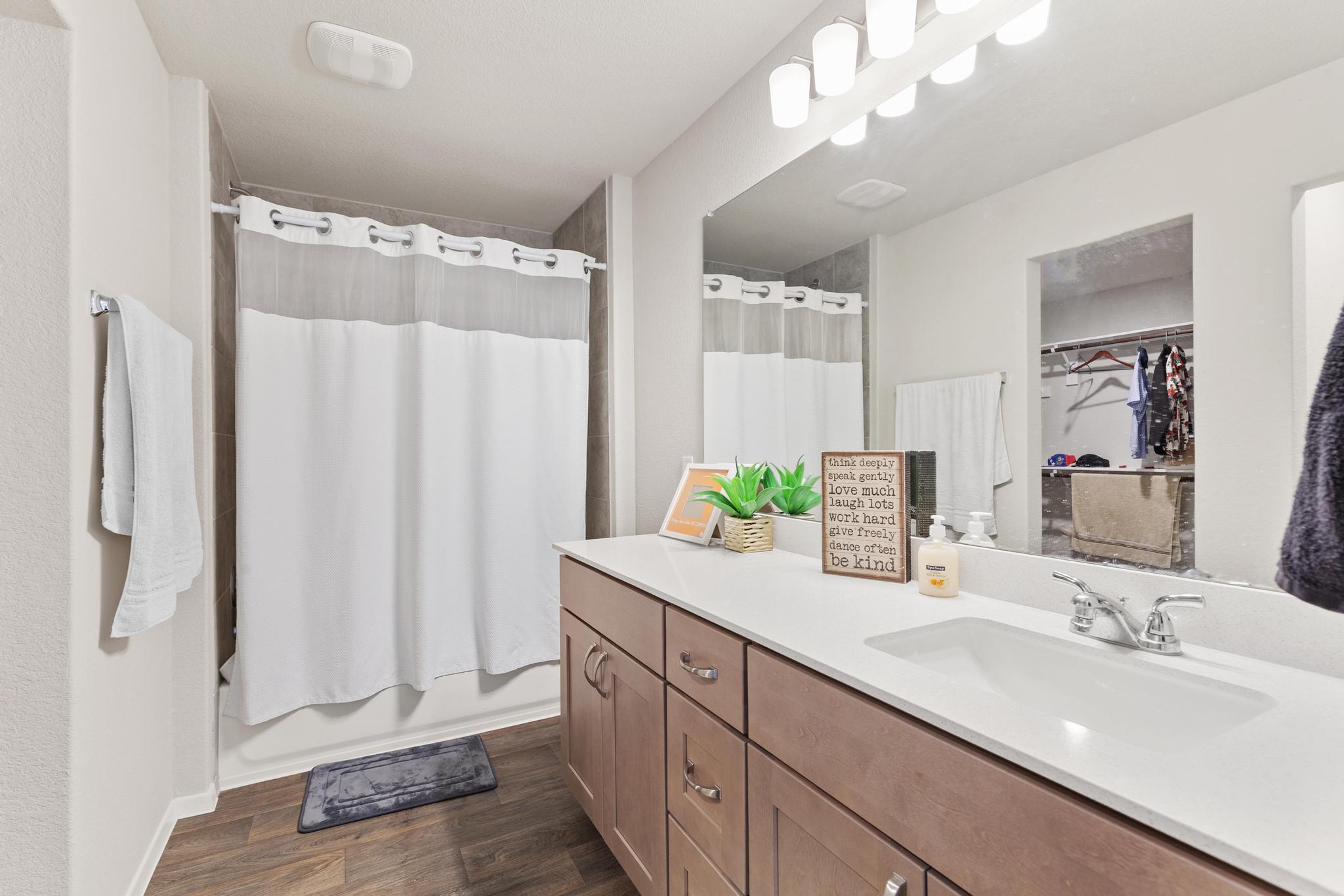 242 Barley Lane Elgin, TX 78621 - Photo 27 of 31 Bathroom featuring a wood-finish floor, a single vanity with a white countertop and integrated sink, a large wall mirror, and a full bathtub with a shower
