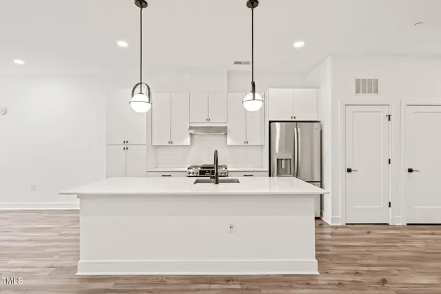 a kitchen with stainless steel appliances granite countertop a refrigerator a sink dishwasher a stove and white countertops with wooden floor