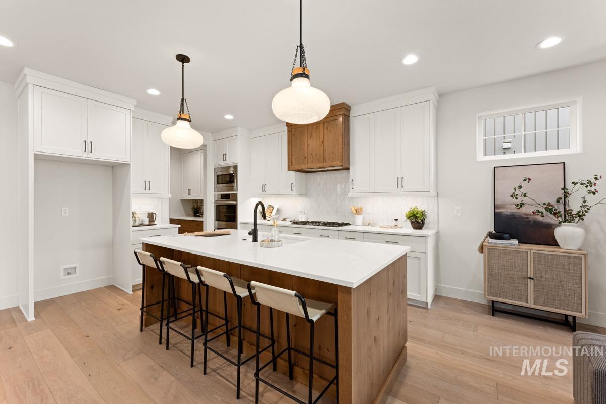 13338 North Spring Creek Way Boise, ID 83714 - Photo 7 of 46 Modern kitchen featuring a large island with seating, light wood-finish flooring, white cabinetry, a wood-paneled range hood, and recessed lighting