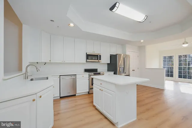 a kitchen with stainless steel appliances granite countertop a stove top oven a sink a refrigerator white cabinets and wooden floor