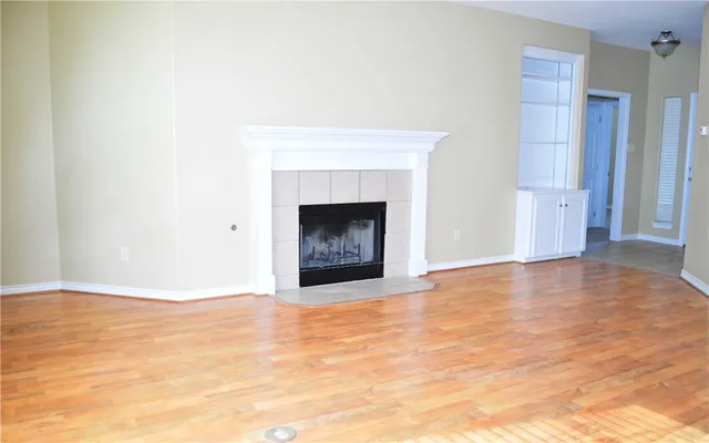 a view of an empty room with wooden floor and a fireplace
