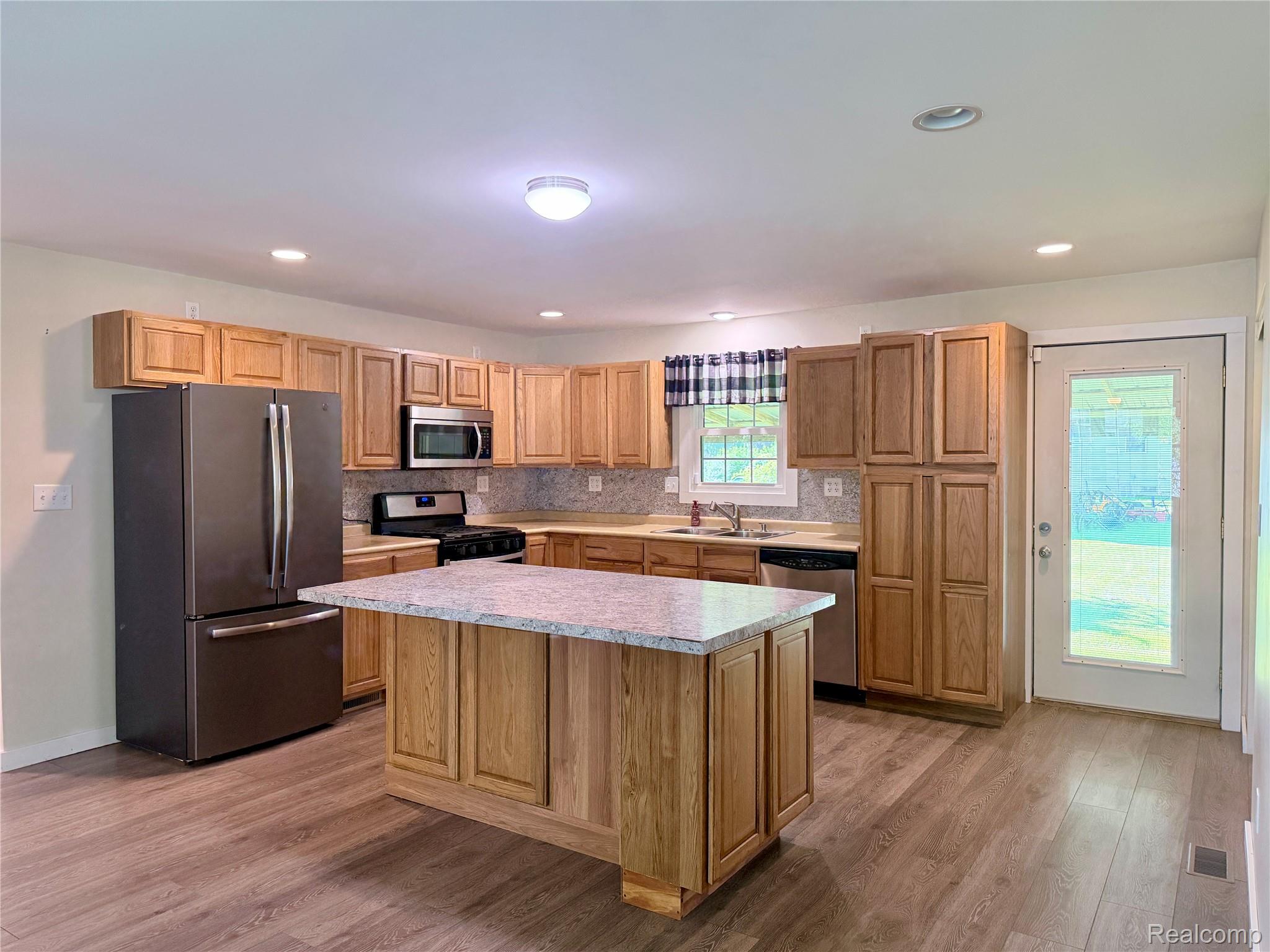 1295 Allen Road Smiths Creek, MI 48074 - Photo 9 of 28 Spacious kitchen featuring warm wood cabinetry, a large center island with white countertop, stainless steel appliances including French-door refrigerator and built-in microwave, wood-finish flooring, and abundant recessed lighting throughout