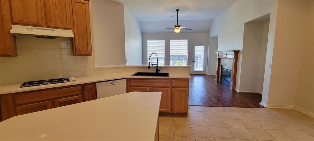 1467 Cattle Baron Court Fairview, TX 75069 - Photo 11 of 32 Kitchen with tasteful backsplash, light countertops, light tile patterned floors, brown cabinetry, and a glass covered fireplace