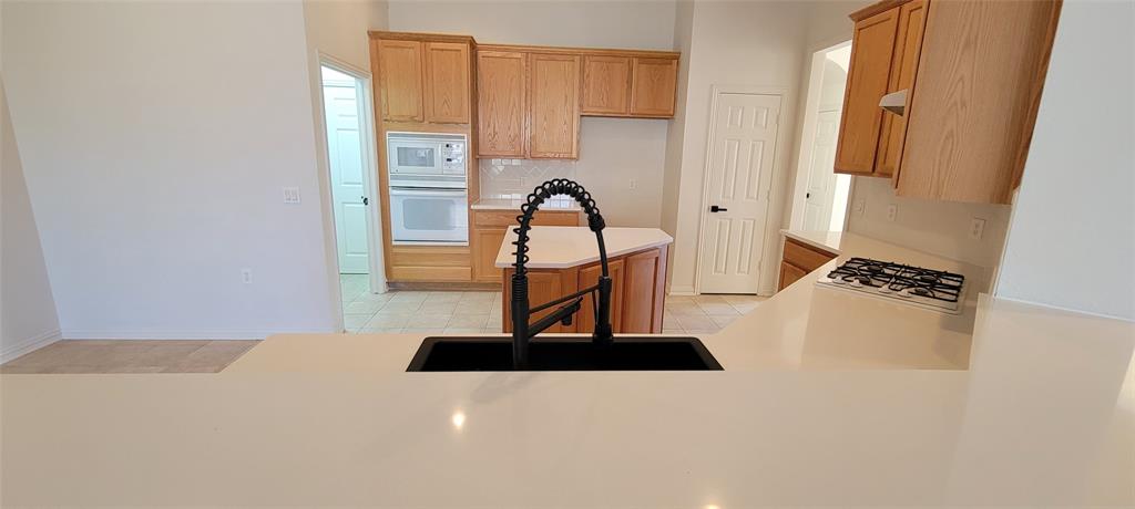 1467 Cattle Baron Court Fairview, TX 75069 - Photo 9 of 32 Kitchen with white appliances, light countertops, light tile patterned floors, backsplash, and brown cabinets