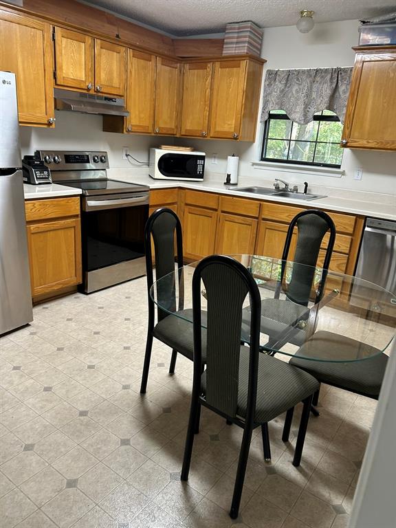 2275 Graham Street Paris, TX 75460 - Photo 6 of 21 Kitchen featuring light countertops, stainless steel appliances, brown cabinetry, a textured ceiling, and under cabinet range hood