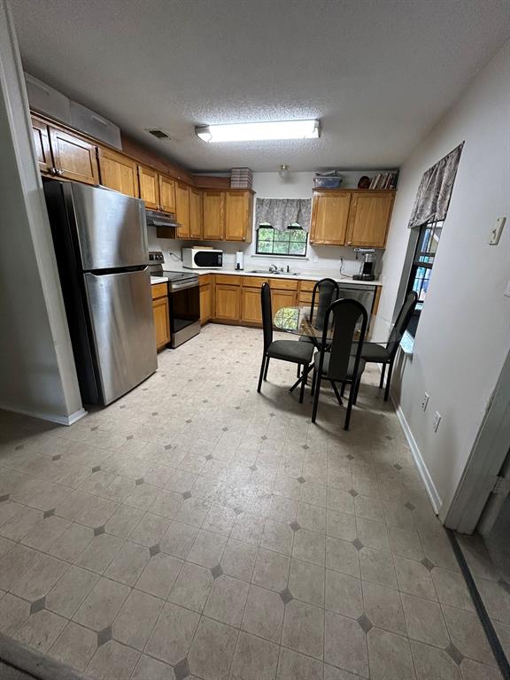 2275 Graham Street Paris, TX 75460 - Photo 7 of 21 Kitchen with stainless steel appliances, light countertops, a textured ceiling, brown cabinets, and light floors