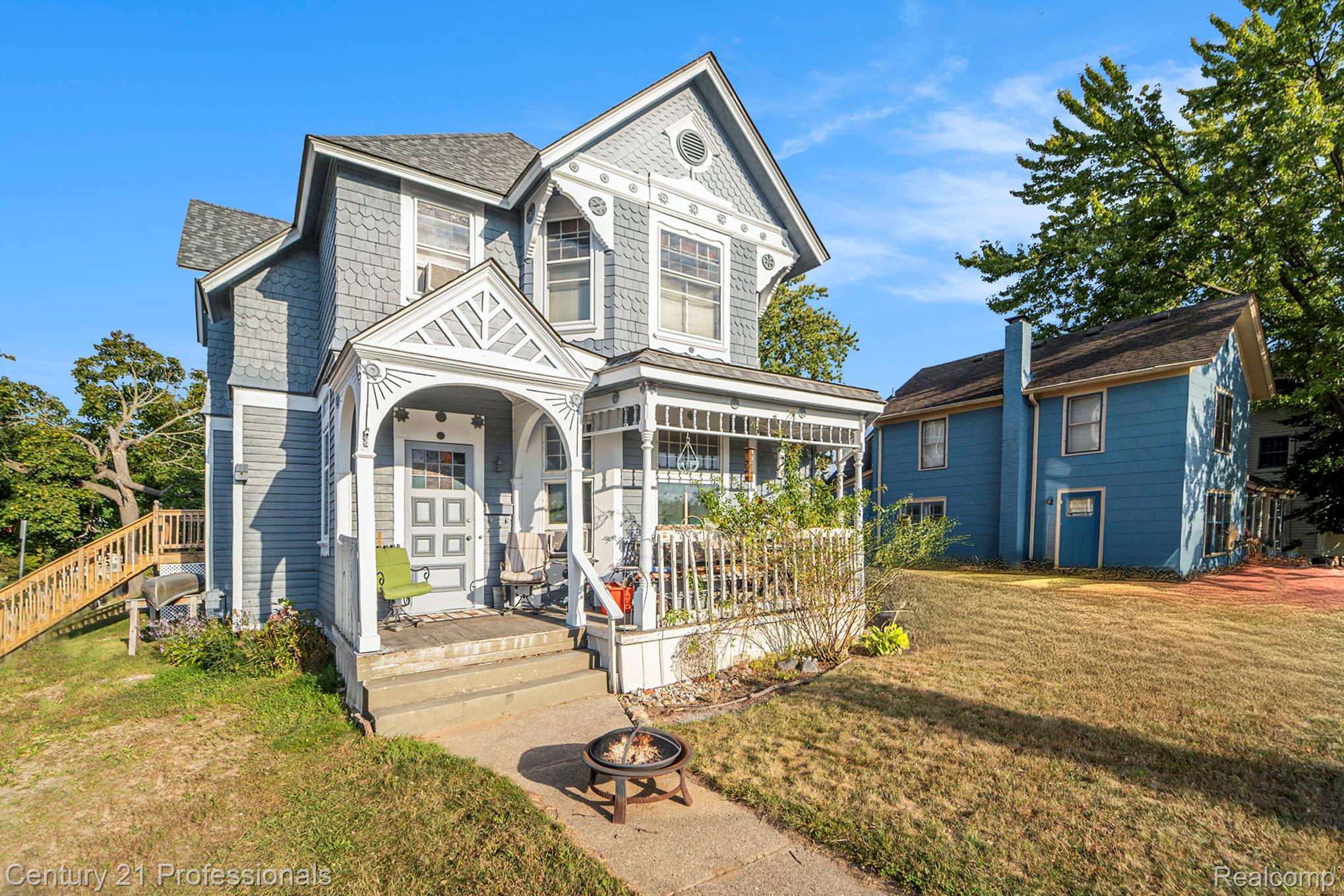 Victorian-style house with a front yard, covered porch, an outdoor fire pit, and roof with shingles