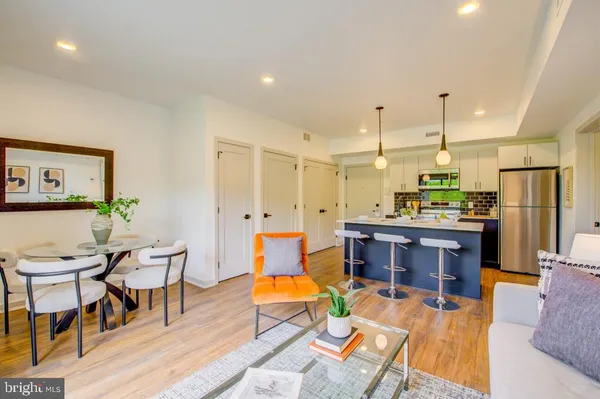 a open kitchen with stainless steel appliances kitchen island granite countertop a refrigerator a stove a dining table and chairs with wooden floor