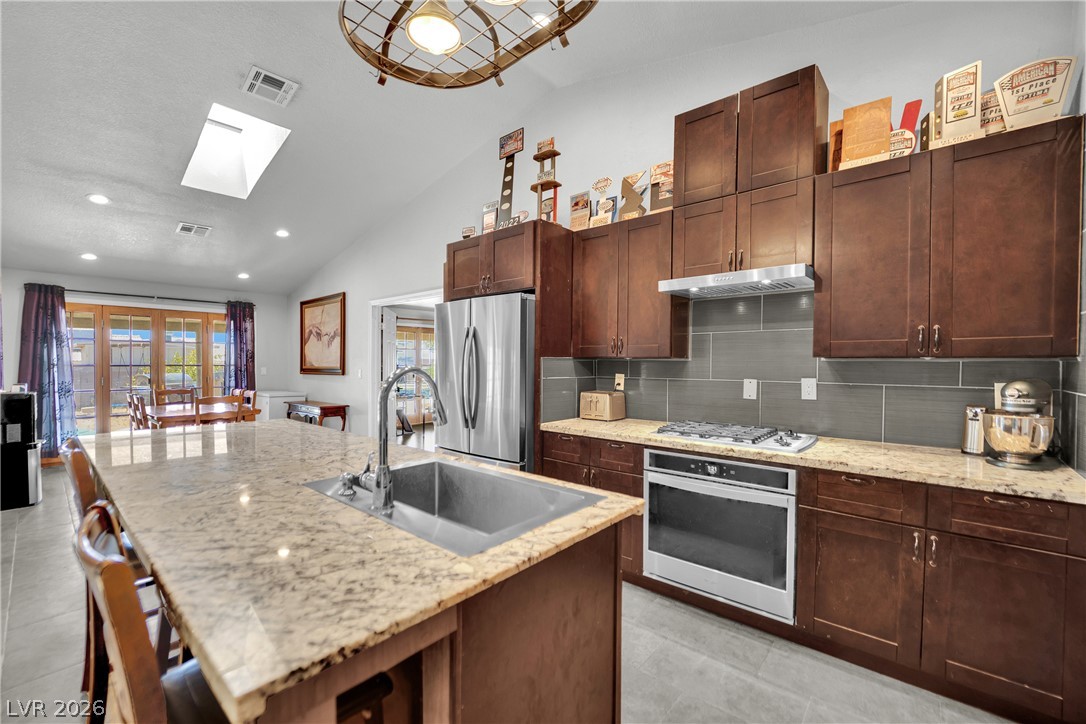 420 North Racetrack Road Henderson, NV 89015 - Photo 18 of 52 A well-appointed kitchen showcasing a spacious island with sink, ample cabinetry, and sleek stainless steel appliances, all beneath a vaulted ceiling with a skylight.