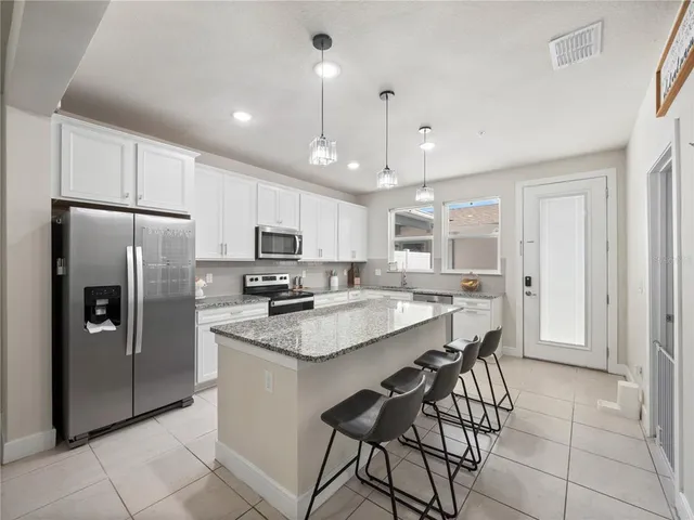 a kitchen with stainless steel appliances granite countertop a refrigerator a sink dishwasher a stove and white cabinets with wooden floor