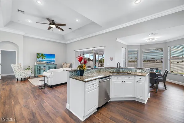 a open kitchen with stainless steel appliances granite countertop a sink dishwasher and white cabinets with wooden floor