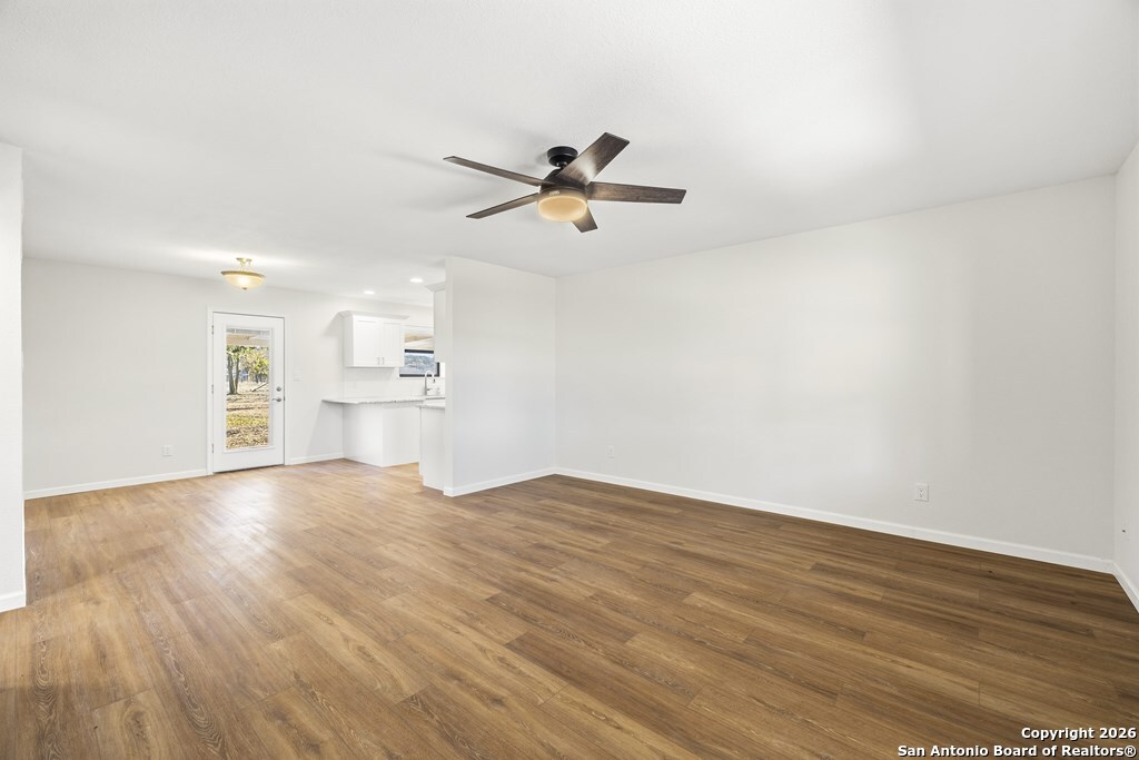 341 Stoneleigh Road Center Point, TX 78010 - Photo 2 of 18 an empty room with wooden floor ceiling fan and windows