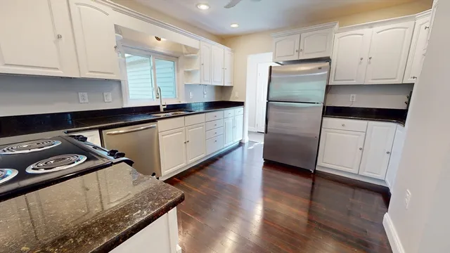 a kitchen with granite countertop a refrigerator stove and white cabinets