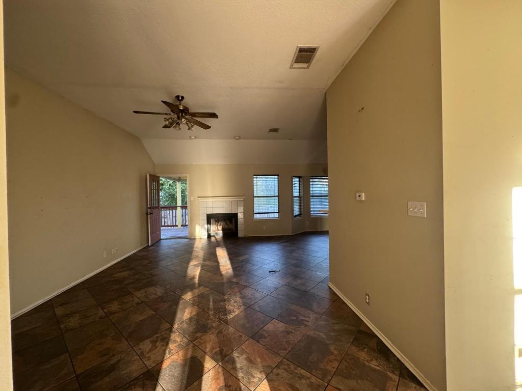 1805 Whirlwind Trail Round Rock, TX 78664 - Photo 5 of 17 Unfurnished living room with a fireplace, vaulted ceiling, a ceiling fan, dark stone finish floors, and a textured ceiling
