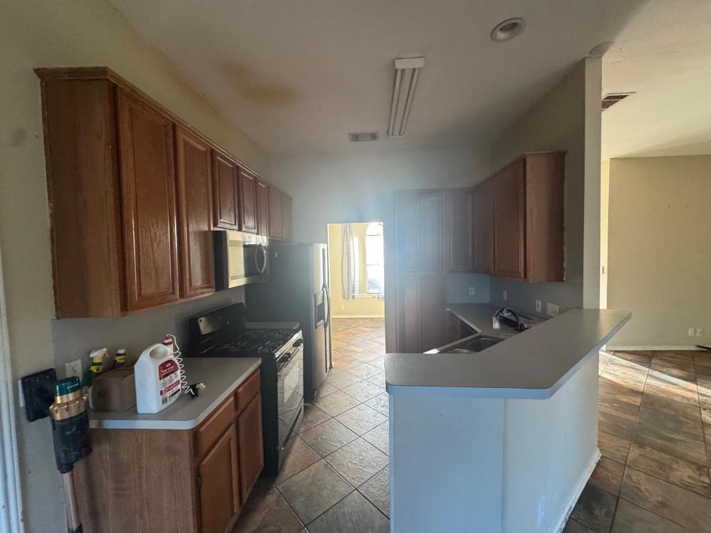 1805 Whirlwind Trail Round Rock, TX 78664 - Photo 6 of 17 Kitchen featuring black gas range, stainless steel microwave, brown cabinets, light countertops, and a peninsula