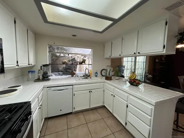 a kitchen with a sink dishwasher and white cabinets with wooden floor