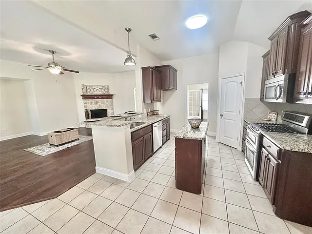 a large kitchen with stainless steel appliances granite countertop a stove top oven a sink dishwasher a dining table and chairs with wooden floor