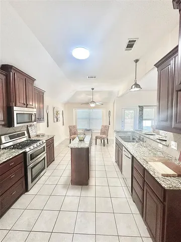 a large kitchen with kitchen island granite countertop lots of counter top space a sink a stove and cabinets