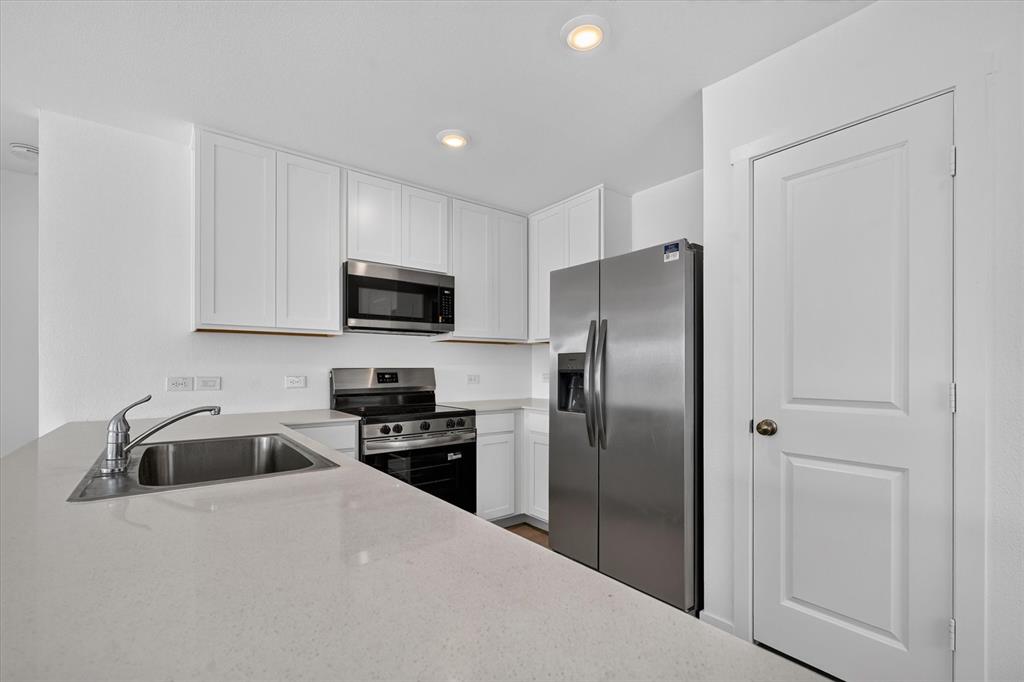White shaker-style cabinetry, stainless steel appliances, dual basin sink with a single-handle faucet, and light-toned countertops