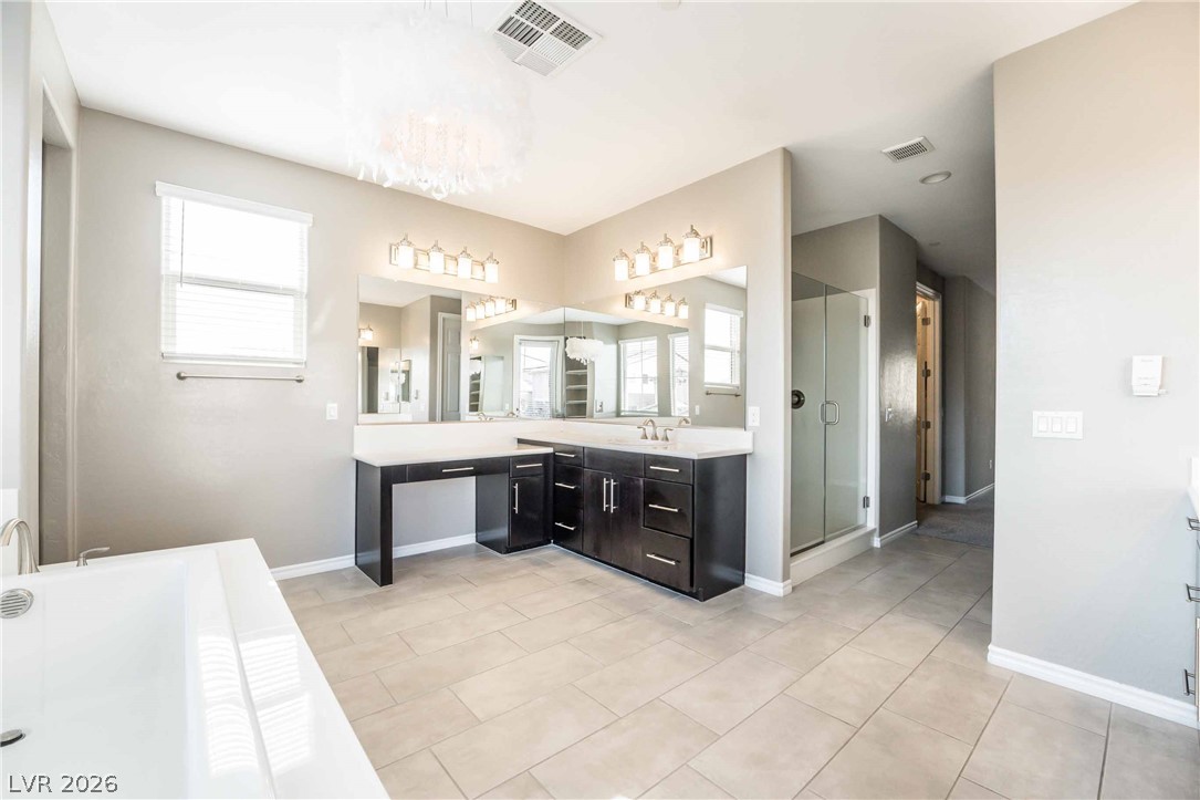 2787 Athens Ridge Drive Henderson, NV 89052 - Photo 17 of 31 Luxurious primary bathroom features a generous soaking tub and spacious vanity area, all illuminated by a contemporary chandelier.