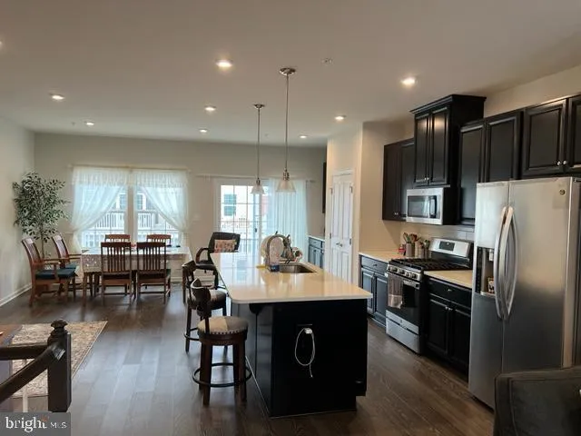 a kitchen with stainless steel appliances kitchen island granite countertop a refrigerator a stove a sink a dining table and chairs with wooden floor