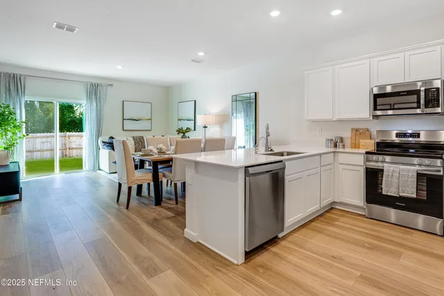 a kitchen with stainless steel appliances granite countertop a stove top oven a sink dishwasher a dining table and chairs with wooden floor