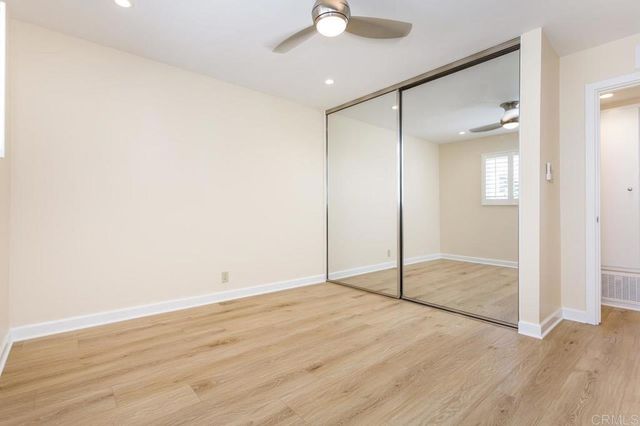 a view of an empty room with wooden floor and a ceiling fan