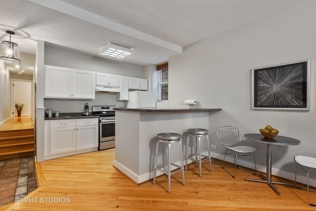 647 West Sheridan Road, Unit 1E Chicago, IL 60613 - Photo 8 of 17 a kitchen with granite countertop a stove top oven a sink dishwasher and white cabinets with wooden floor