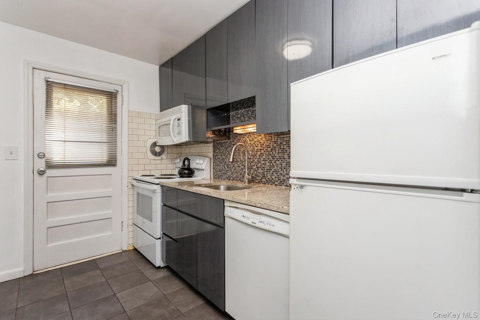 51 Cross Street, Unit 3A Yonkers, NY 10708 - Photo 7 of 17 Kitchen with white appliances, dark tile patterned flooring, backsplash, light stone countertops, and modern cabinets