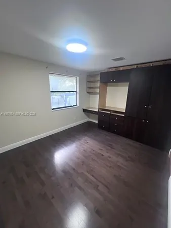 an empty room with wooden floor cabinet and windows