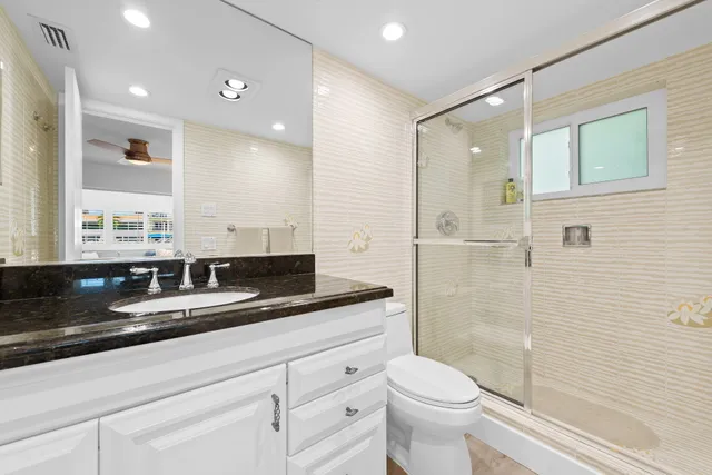 a bathroom with a granite countertop sink a toilet a mirror and shower