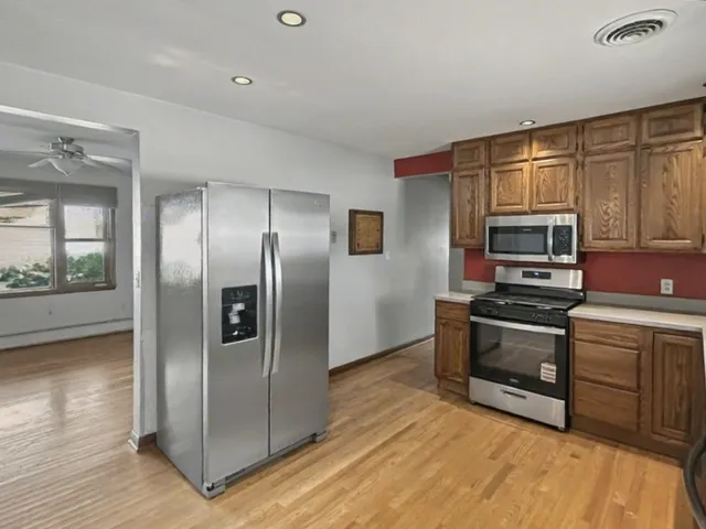 a kitchen with stainless steel appliances granite countertop a refrigerator a stove and a sink with wooden floor