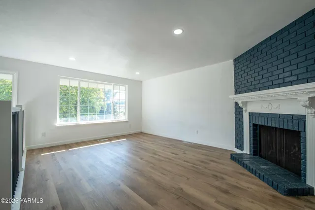 an empty room with wooden floor fireplace and windows