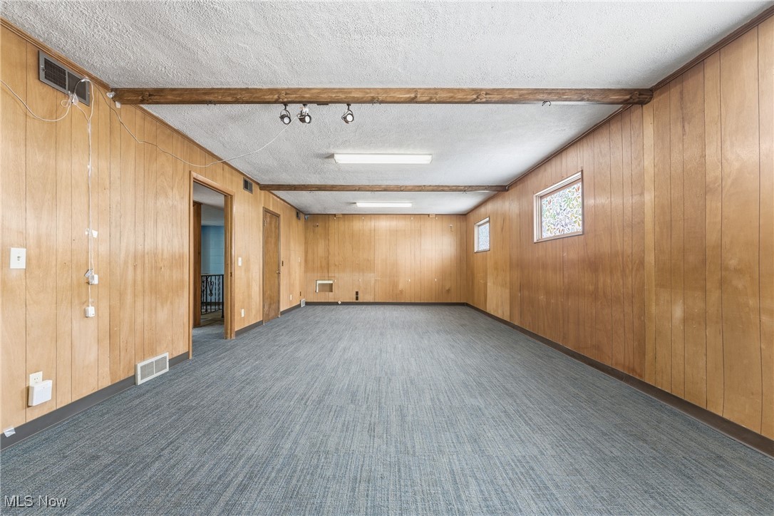 1817 Fulton Road Northwest Canton, OH 44709 - Photo 9 of 25 Unfurnished room featuring wooden walls, a textured ceiling, beamed ceiling, and dark carpet