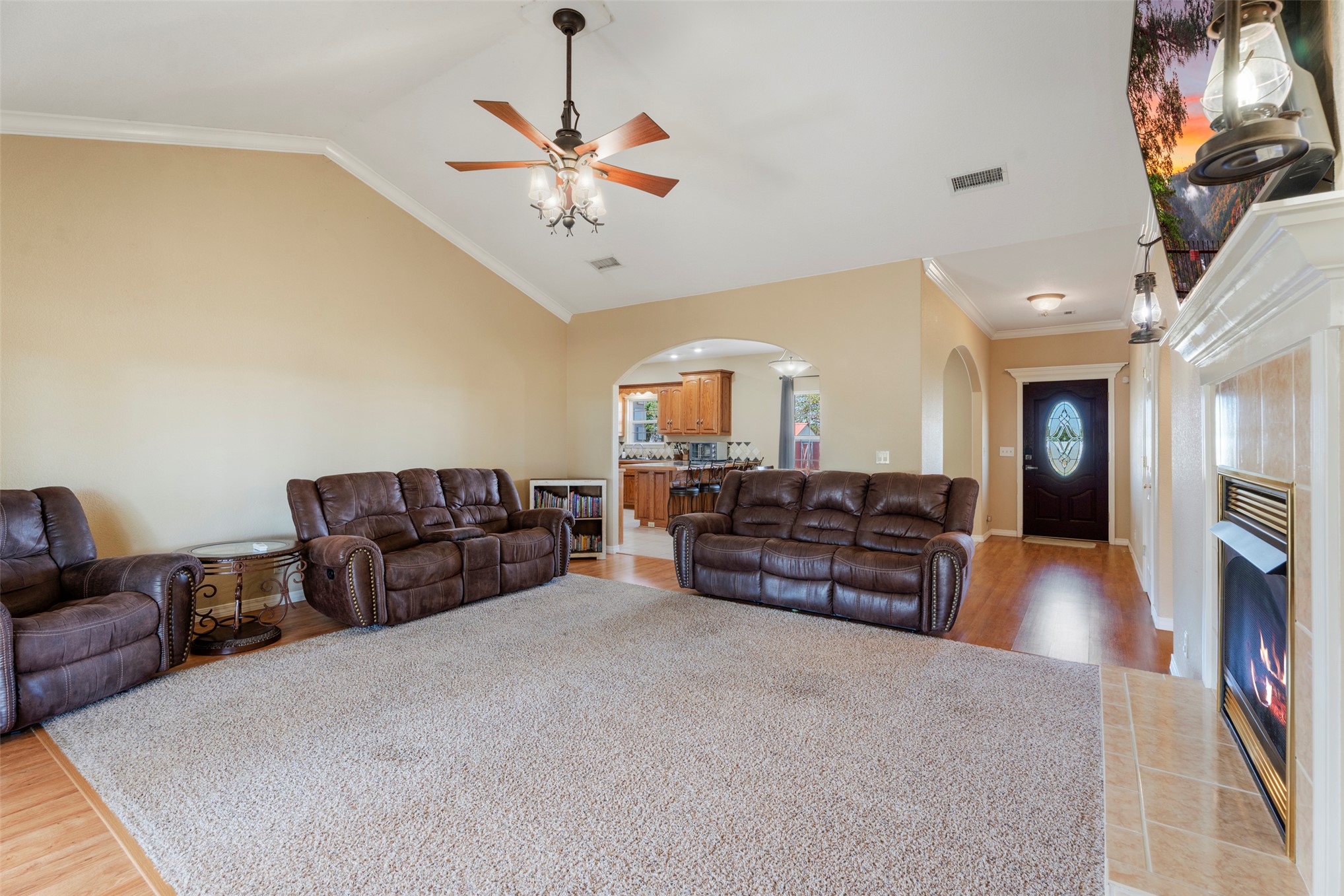 20233 East 570 Road Colcord, OK 74338 - Photo 9 of 39 Vaulted ceiling with a ceiling fan, hardwood-finish flooring, tiled fireplace, decorative front door, and arched entryways