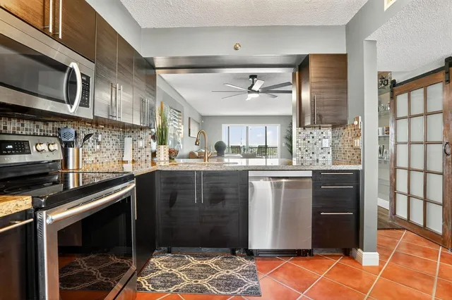 a kitchen with stainless steel appliances granite countertop a refrigerator a sink dishwasher a stove and white countertops with wooden floor