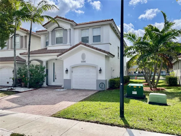 a view of a white house next to a yard with palm trees