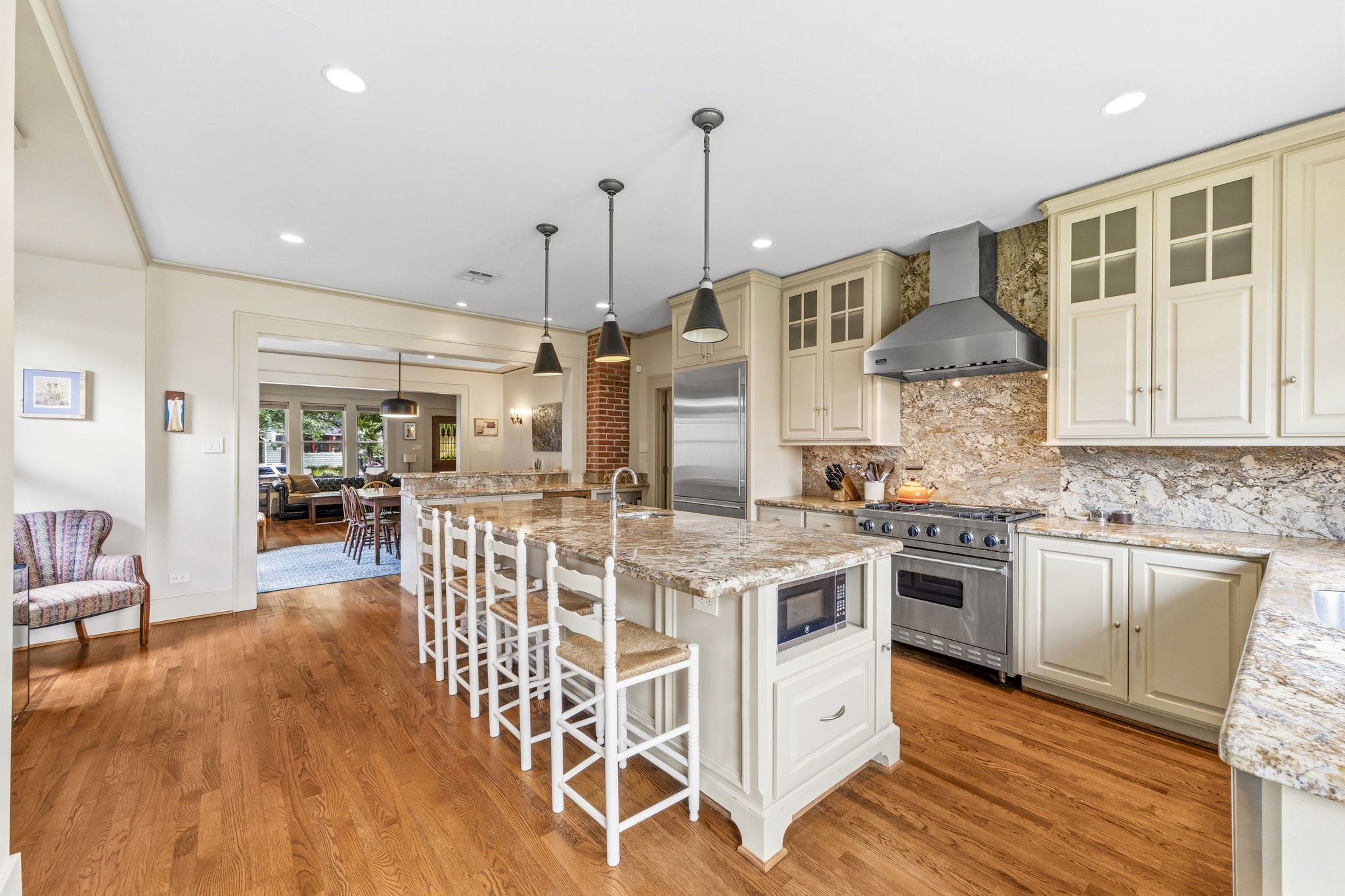 1521 Kipling Street Houston, TX 77006 - Photo 16 of 35 This spacious kitchen features a large island with seating, granite countertops, stainless steel appliances, and elegant pendant lighting. It seamlessly connects to a cozy living area with ample natural light.