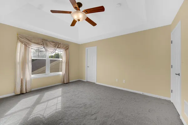 an empty room with chandelier fan and windows