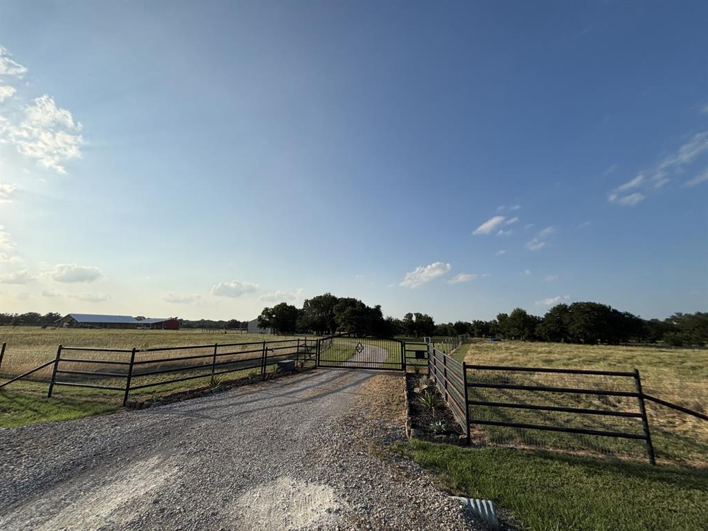 View of dirt / gravel driveway featuring a view of countryside and a gate