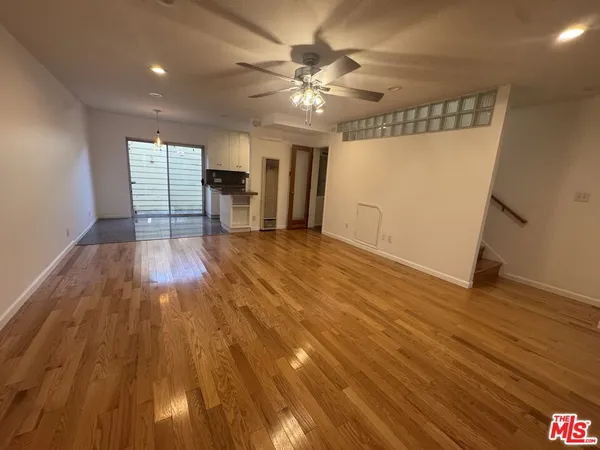 a view of an empty room with wooden floor and a ceiling fan