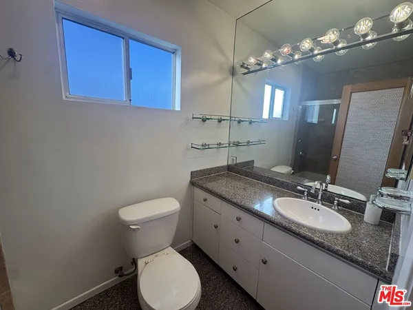a bathroom with a granite countertop toilet a sink and a mirror