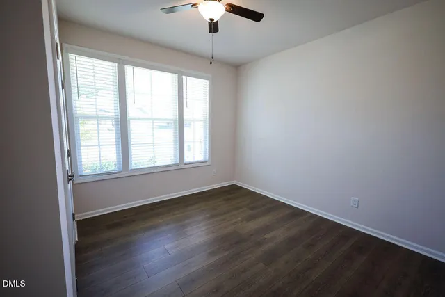 an empty room with wooden floor chandelier fan and windows