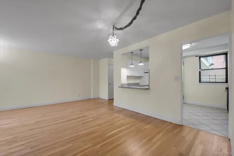 a view of empty room with wooden floor and kitchen view