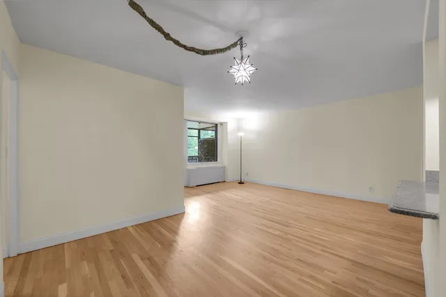 an empty room with wooden floor chandelier and windows
