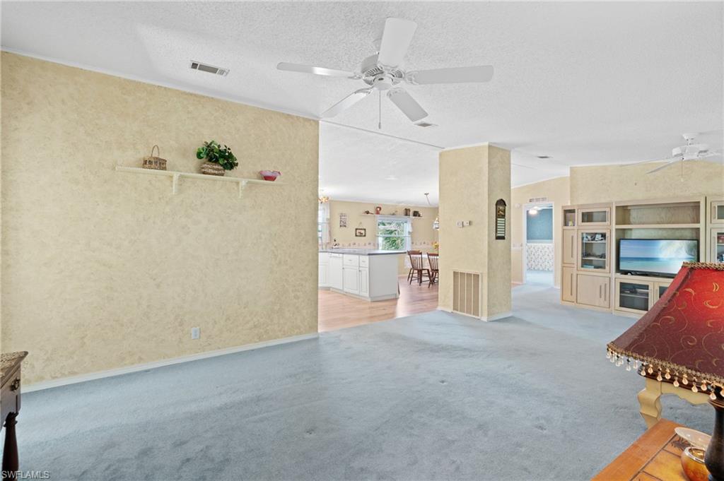 278 Riverwood Road Naples, FL 34114 - Photo 11 of 43 Unfurnished living room featuring visible vents, light carpet, a textured ceiling, and a ceiling fan