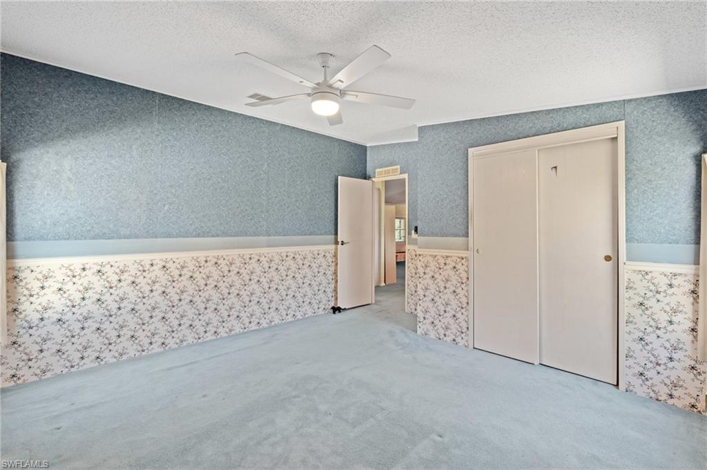 278 Riverwood Road Naples, FL 34114 - Photo 14 of 43 Unfurnished bedroom featuring a ceiling fan, wallpapered walls, a closet, a textured ceiling, and carpet flooring